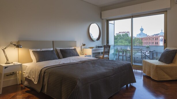 Una moderna camera d'hotel con un letto grande, una scrivania, una sedia e un balcone che offre vista su un edificio a cupola.