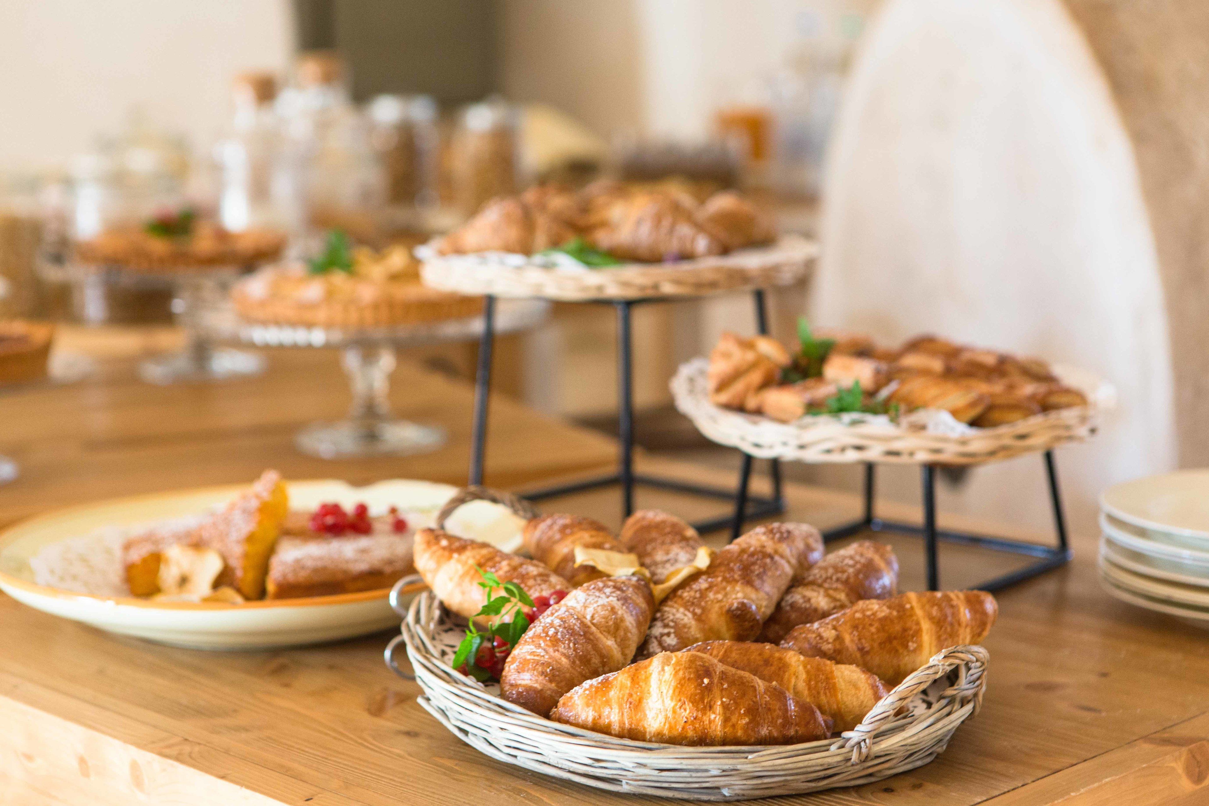 Ein reichhaltiges Buffet mit verschiedenen Backwaren und Brot, darunter Croissants und ein Obstkuchen, präsentiert auf Serviceständern und in einer Korb.