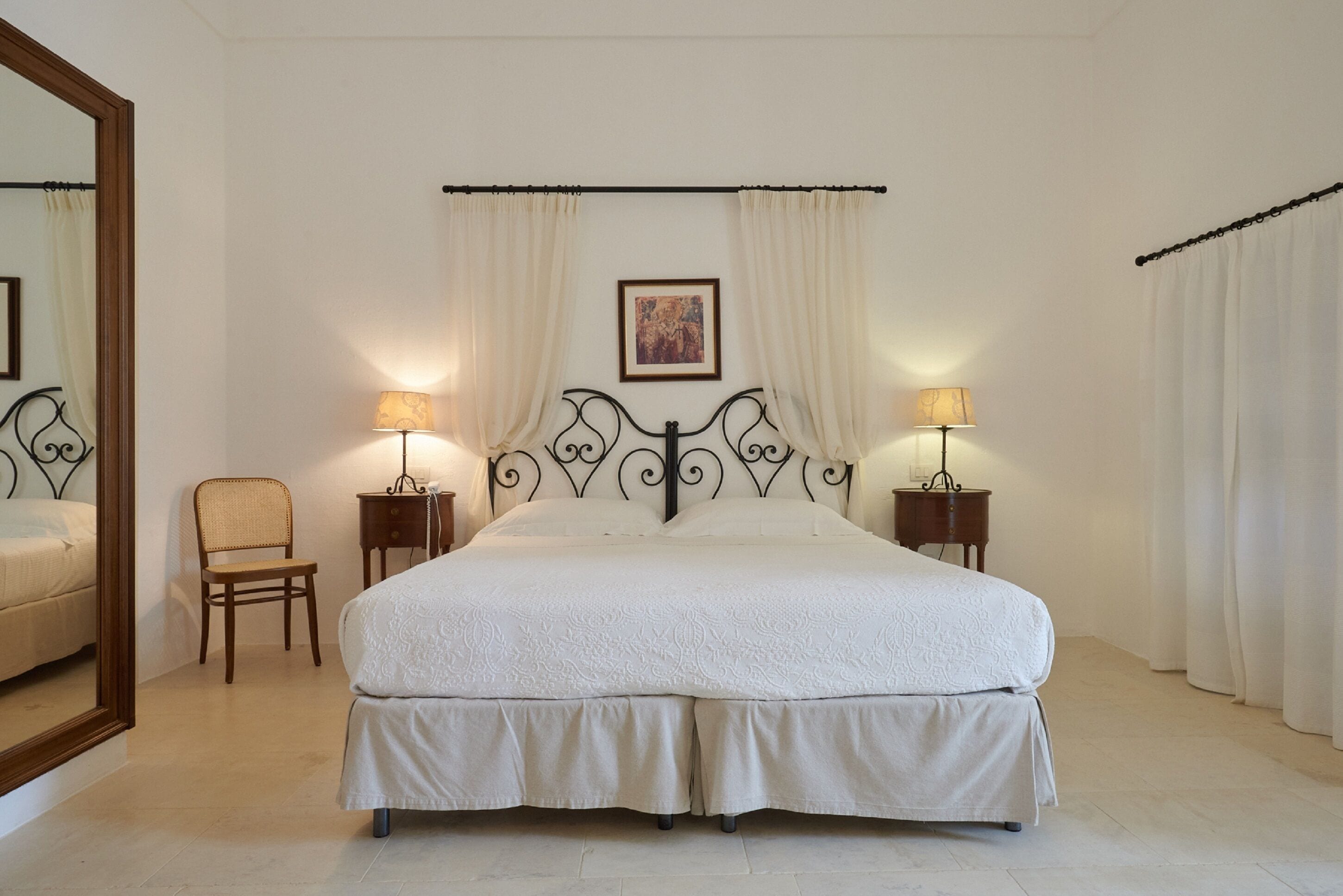 A neatly arranged bedroom with a large bed, two bedside tables with lamps, a chair, and a framed picture on the wall.