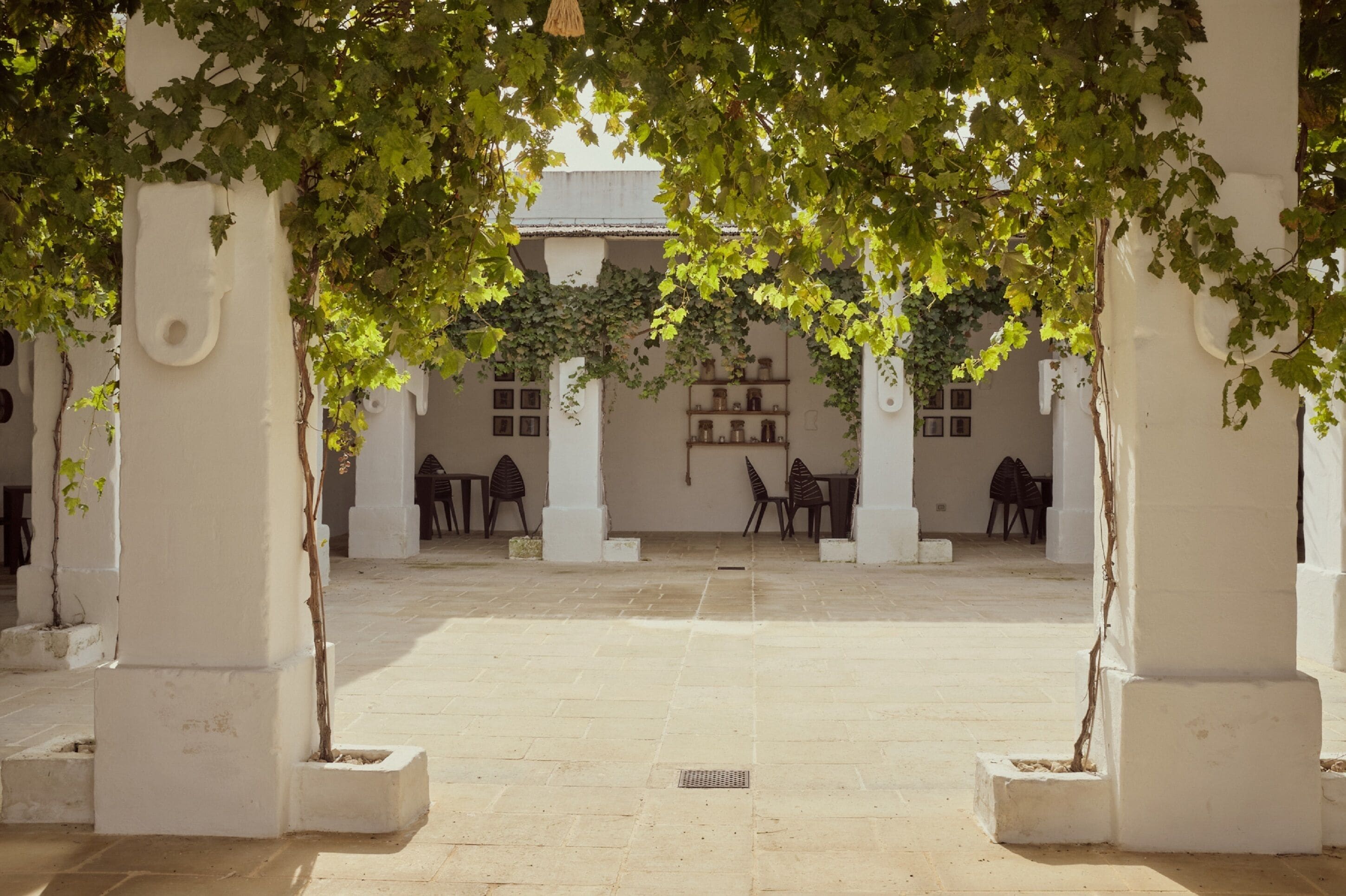 Une cour dotée de colonnes blanches, d’un sol carrelé et d’un espace de repos abrité, avec des chaises et des tables.