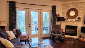 Una sala de estar con sofá, sillón, mesa de centro de vidrio y chimenea.