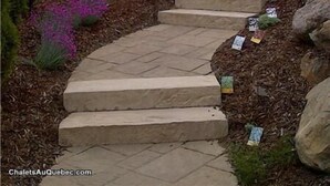 Un sendero de piedra que asciende una escalera, rodeado de vegetación y una valla.