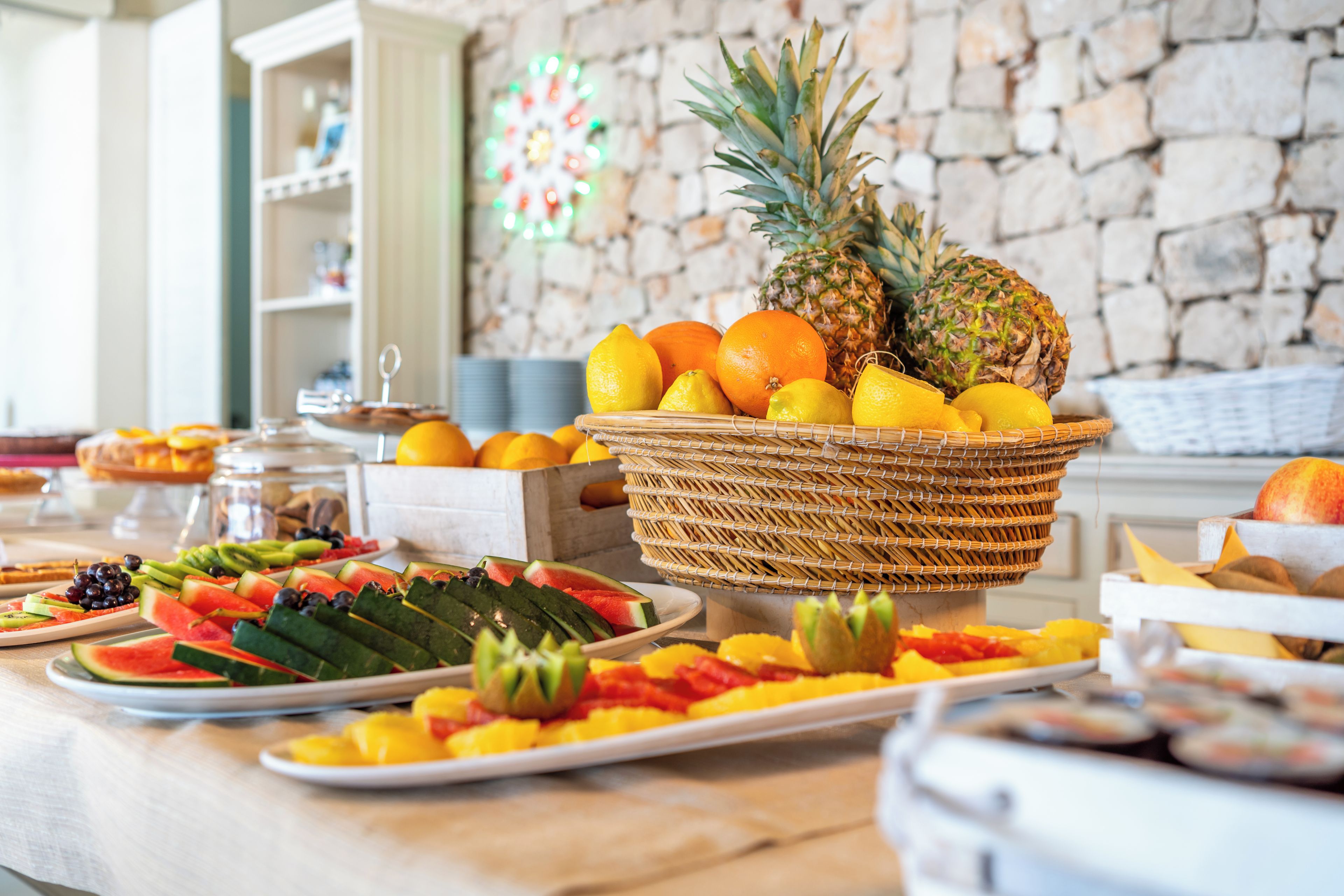 A buffet table with a variety of fruits and a stone wall in the background.