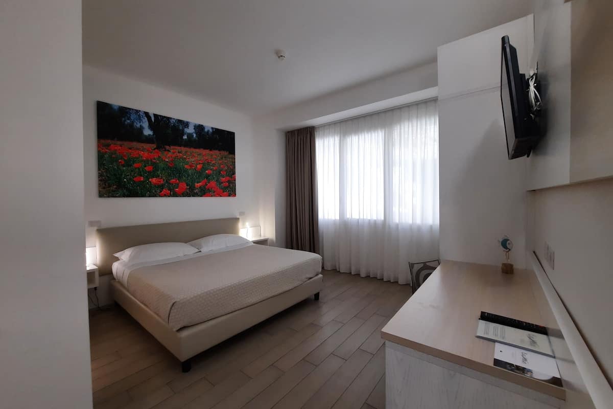Ein Hotelzimmer mit einem Bett, einem Schreibtisch, einem Fernseher und einem Blumenbild.