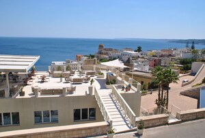 Una terrazza sul tetto con posti a sedere all'aperto, vista sul mare e sullo sfondo un mix di edifici tradizionali e moderni.