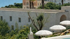 A pool area with a view of a Mediterranean-style building and the sea. - Est Hotel (Santa Cesarea Terme)