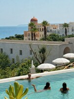 Zona de piscina con vista a un edificio de estilo mediterráneo y al mar.