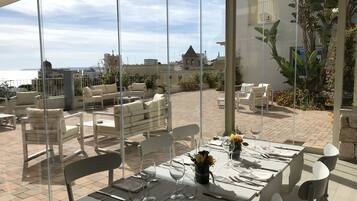 Ein Dachterrasse-Essbereich mit Tischen für zwei Personen, mit Blick auf Stadt und Meer.