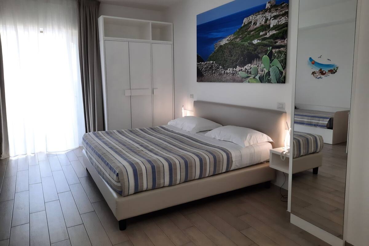 Ein Schlafzimmer mit Bett, Nachttisch, Kleiderschrank und einem Gemälde einer Küstenlandschaft.