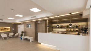 A modern bar area with a white reception desk, seating area with chairs, and a wall of liquor bottles. - Est Hotel (Santa Cesarea Terme)
