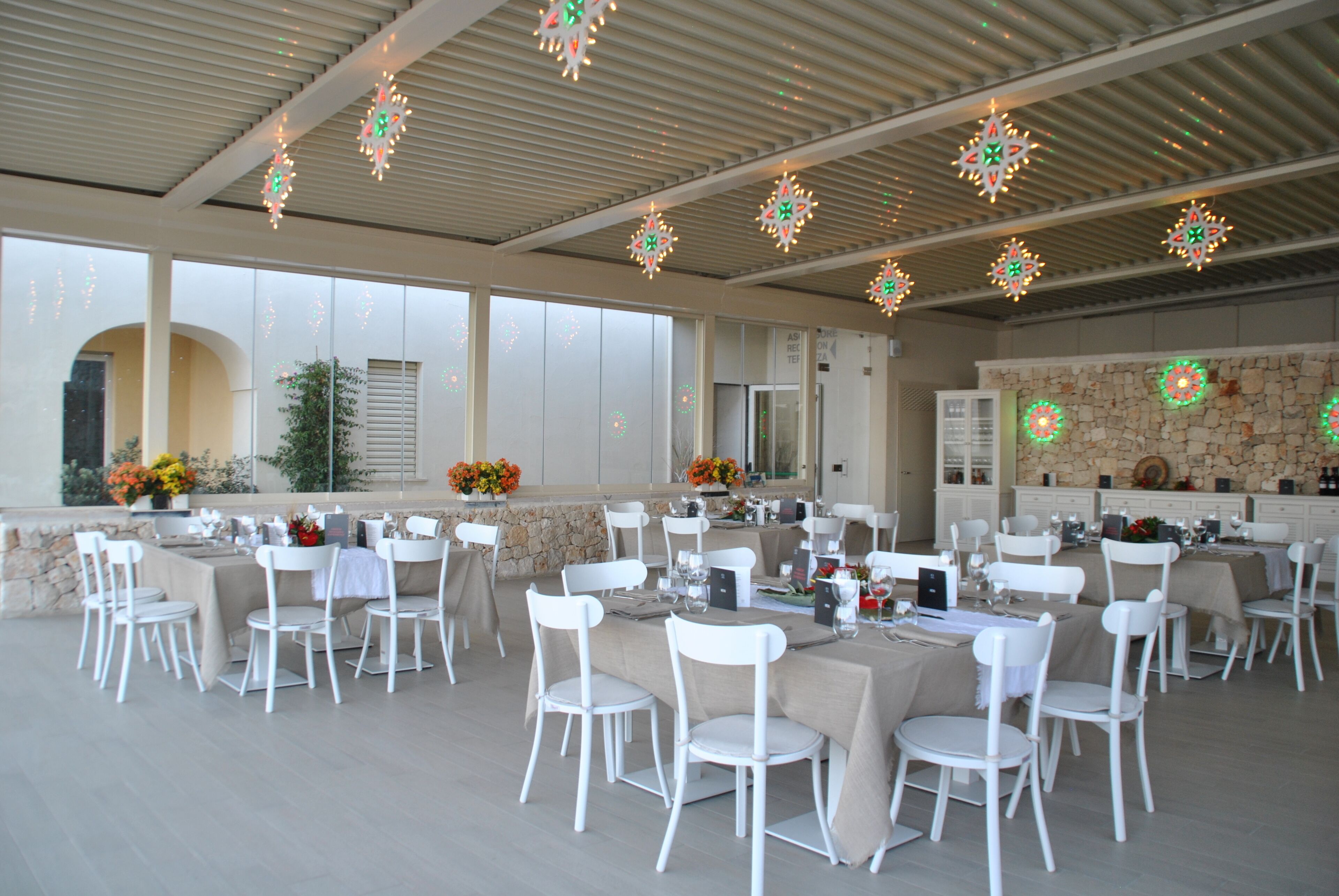 A spacious outdoor dining area with white chairs and tables, decorated with hanging lights.