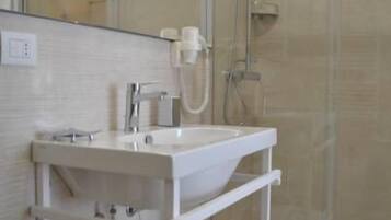 Un baño moderno con ducha de vidrio, lavamanos blanco con espejo y un perchero para toallas.