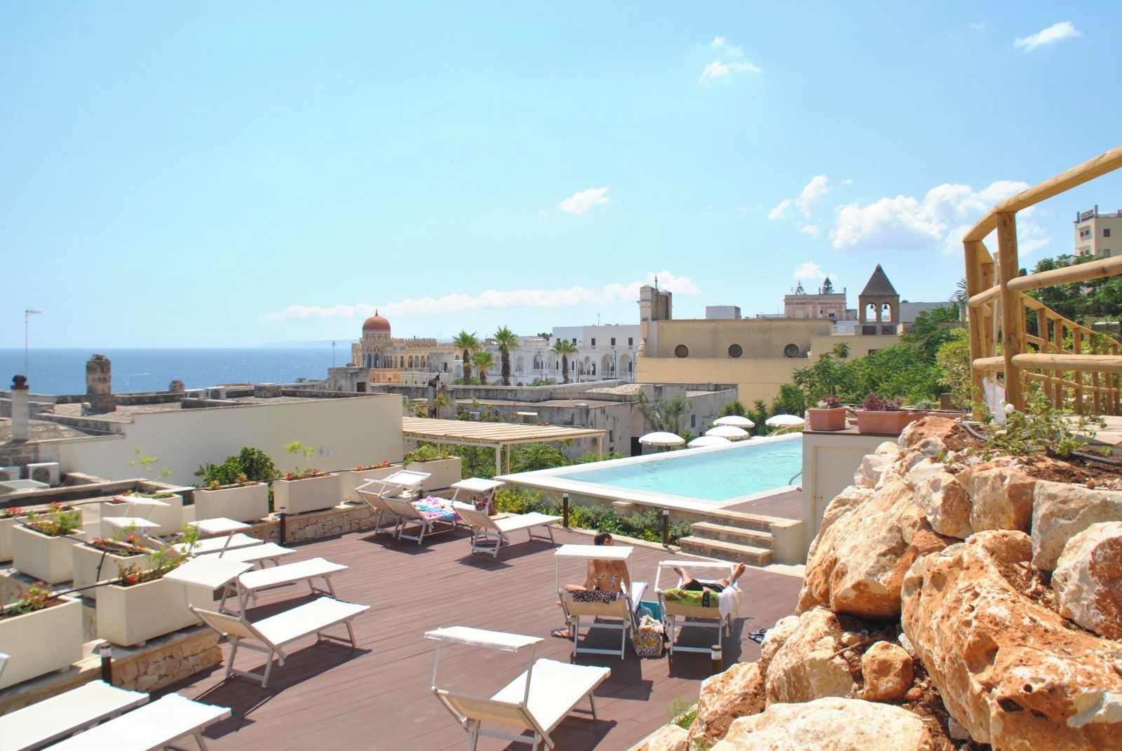 A rooftop pool area with lounge chairs and a view of the sea and historic buildings.