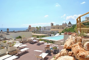 A rooftop pool area with lounge chairs and a view of the sea and historic buildings. - Est Hotel (Santa Cesarea Terme)