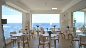 A spacious dining area with multiple tables and chairs, large windows offering a view of the city and the sea, and a modern interior design. - Est Hotel (Santa Cesarea Terme)