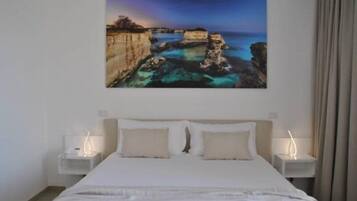 Quarto com cama, duas mesas de cabeceira e um quadro de paisagem costeira.