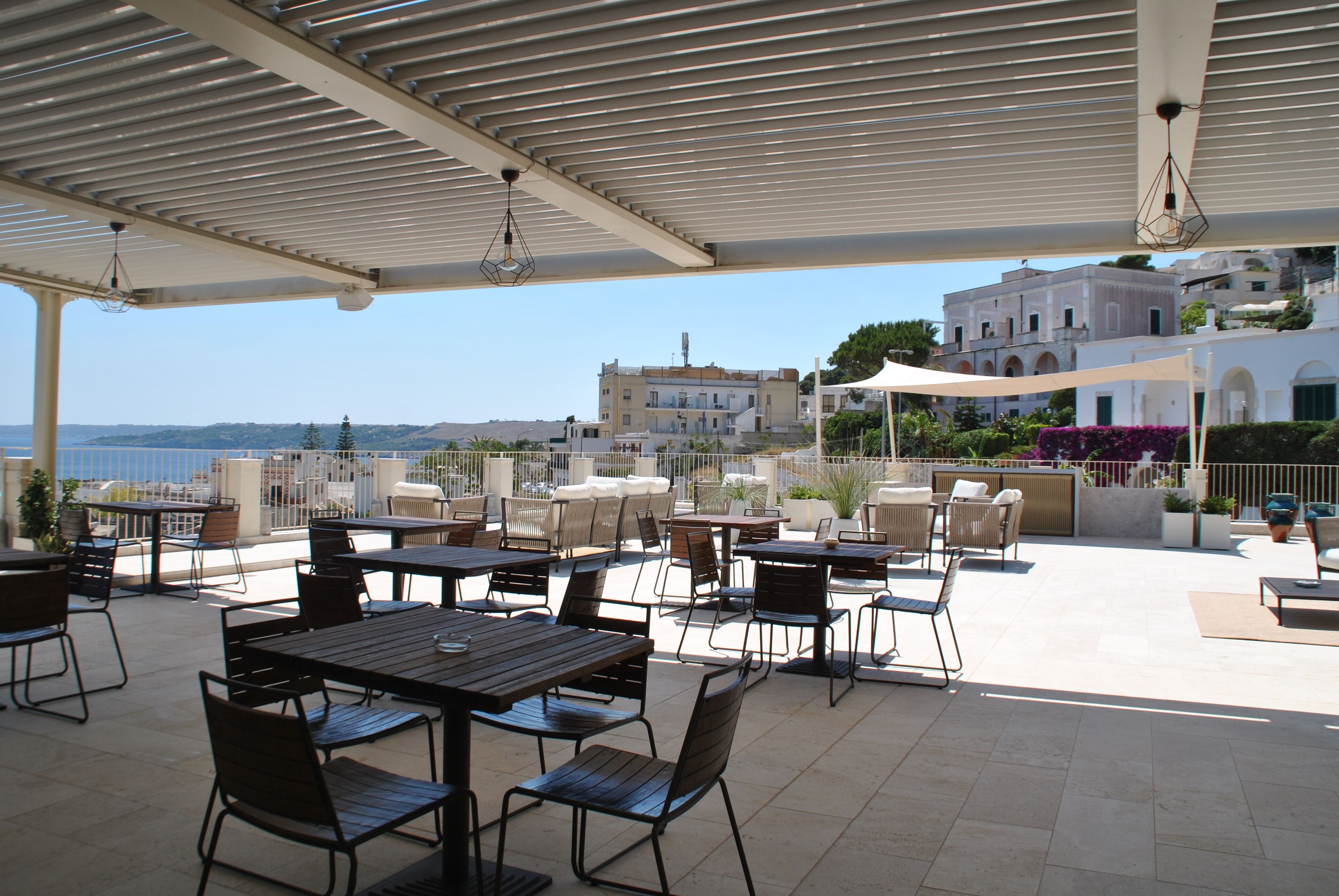 An outdoor patio with tables and chairs, overlooking a coastal cityscape.