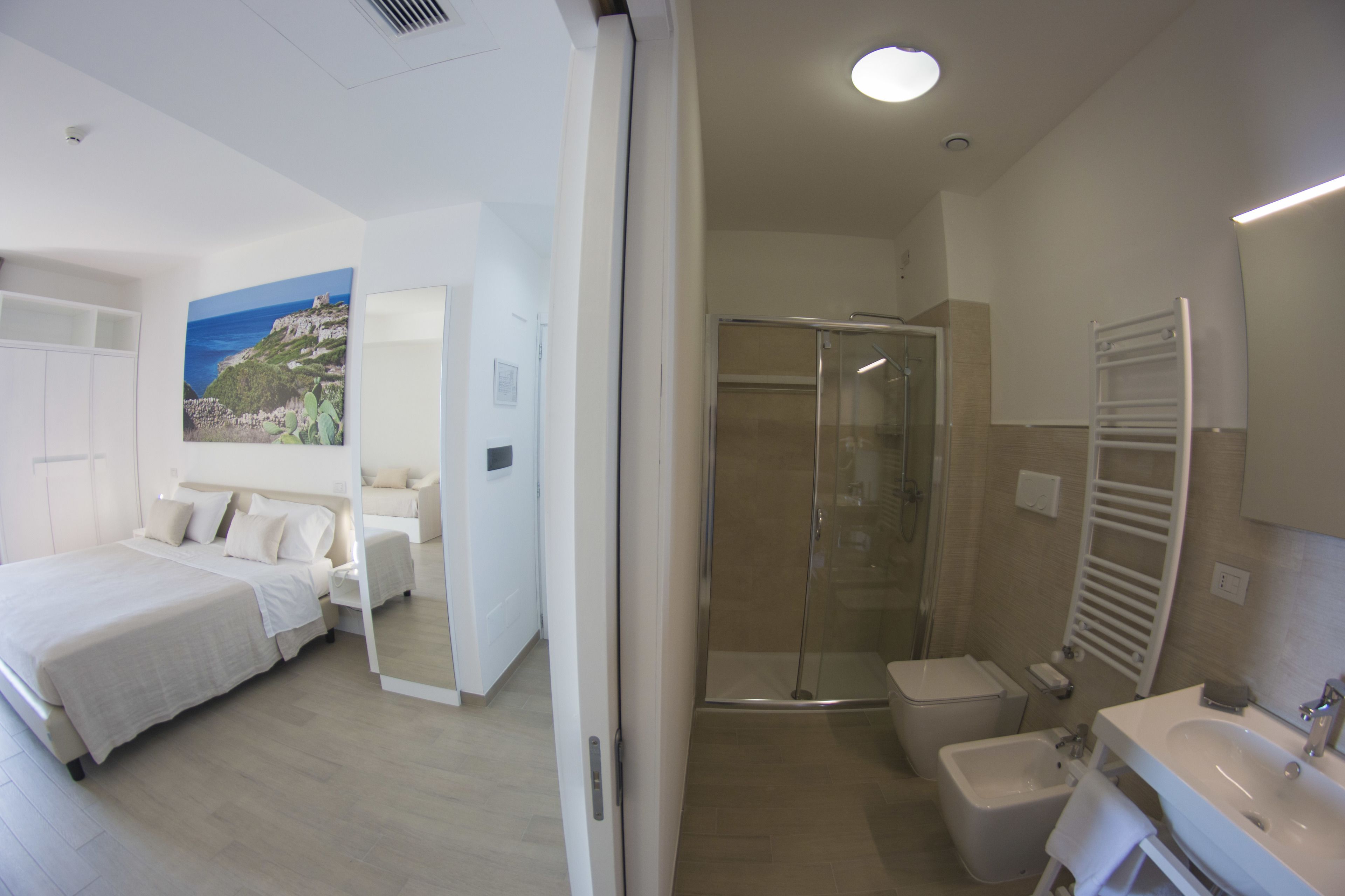 A modern hotel room with a large bed, a shower, a bidet, and a bathroom with a sink and mirror.