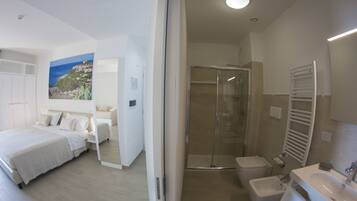 A modern hotel room with a large bed, a shower, a bidet, and a bathroom with a sink and mirror.