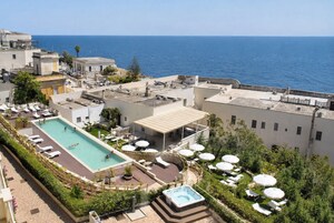 A rooftop pool area with lounge chairs and umbrellas, overlooking a body of water.