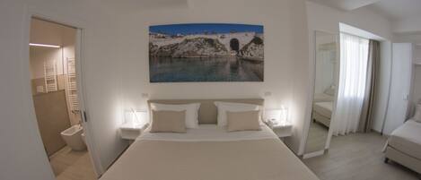 A spacious bedroom with a large bed, bedside tables, and a painting of a bridge over water.