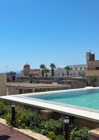 A rooftop pool with a clear view of a historic building with a dome and arches in the background.