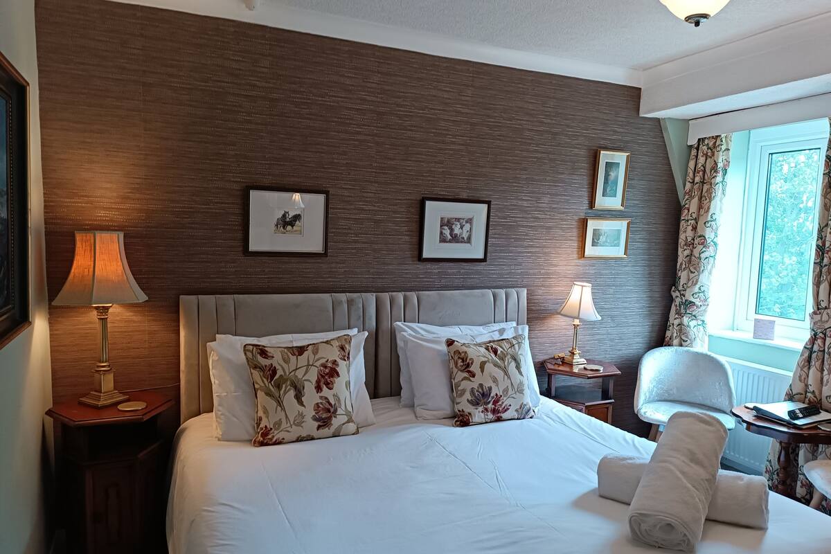 Quarto de hotel com uma cama grande, duas mesas de cabeceira, uma cadeira e uma janela com cortinas.