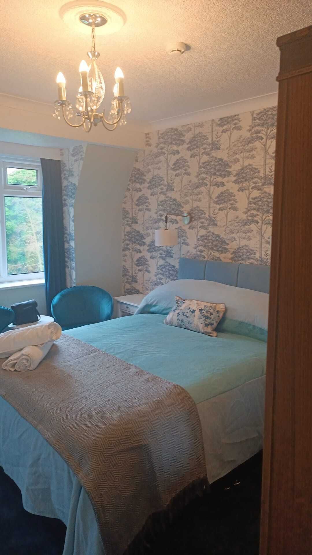 Een slaapkamer met een bed, een stoel, een raam en een kroonluchter.