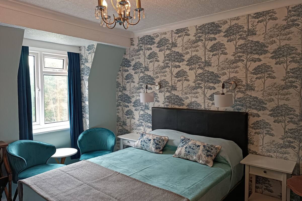 Quarto com cama, duas cadeiras, uma mesinha, um criado-mudo e um candelabro.