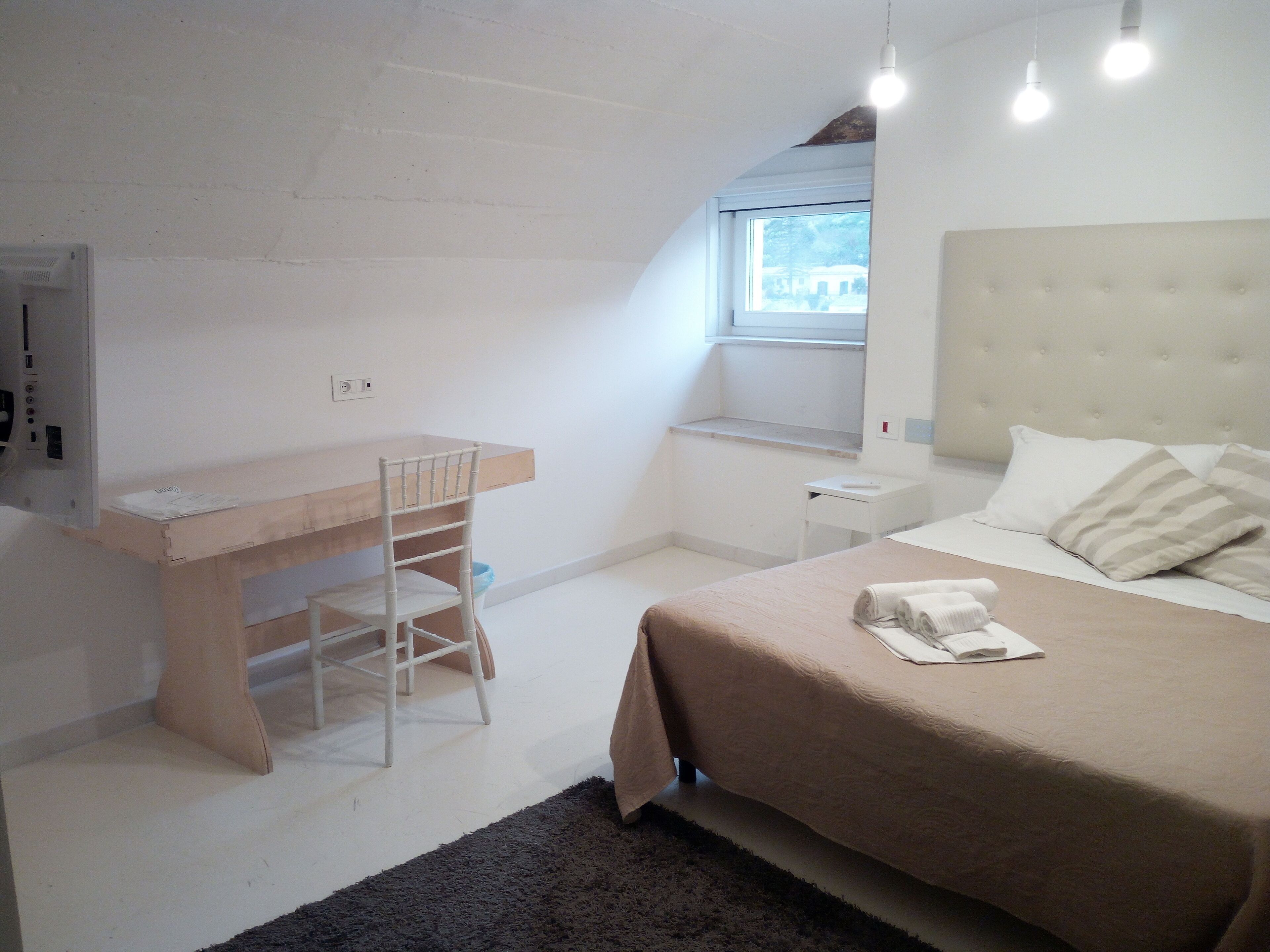 A bedroom with a bed, a desk, a chair, a window, and a radiator.