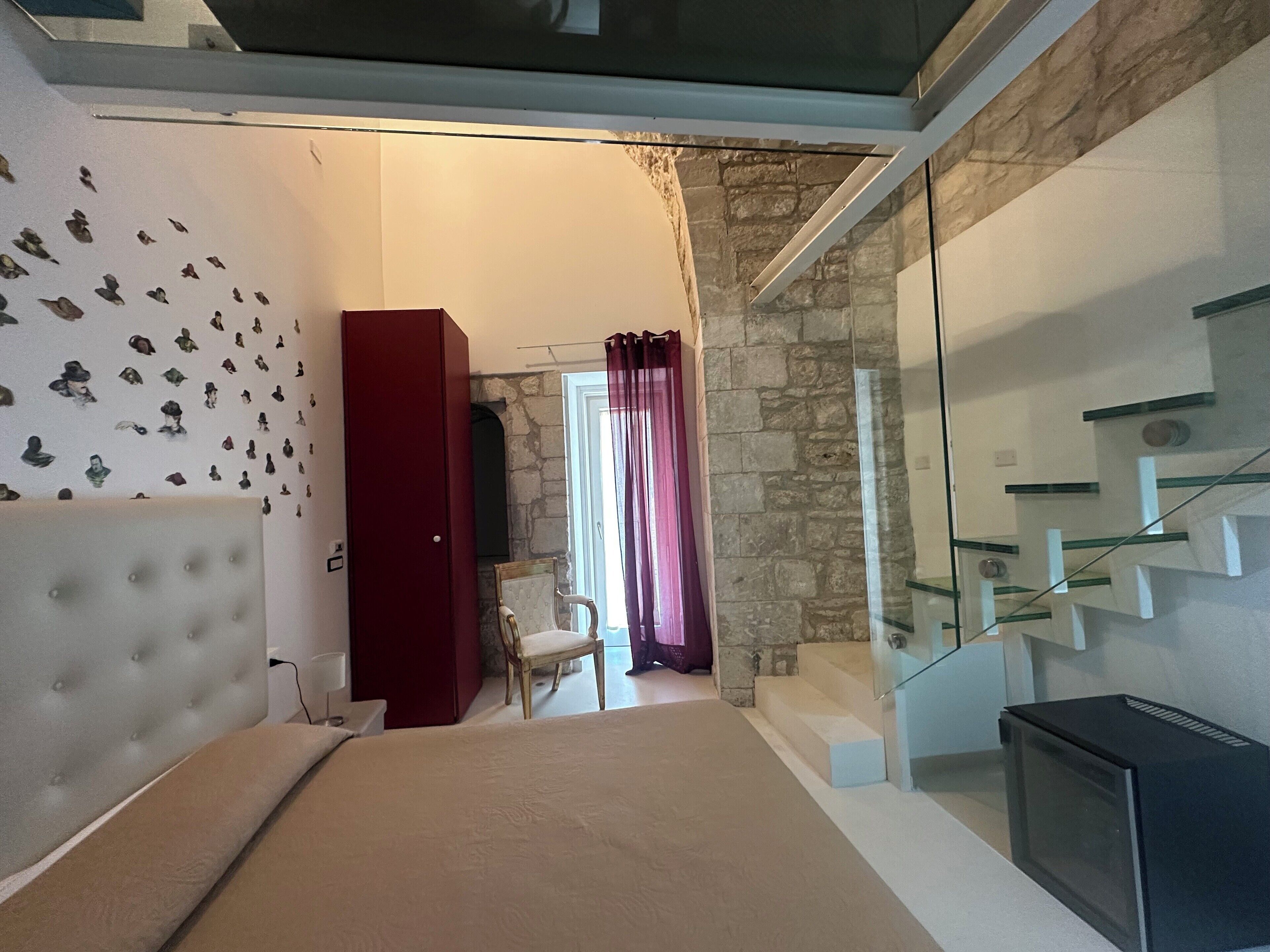 Een slaapkamer met een bed, een rode garderobe, een stoel en een trap met glazen balustrades.