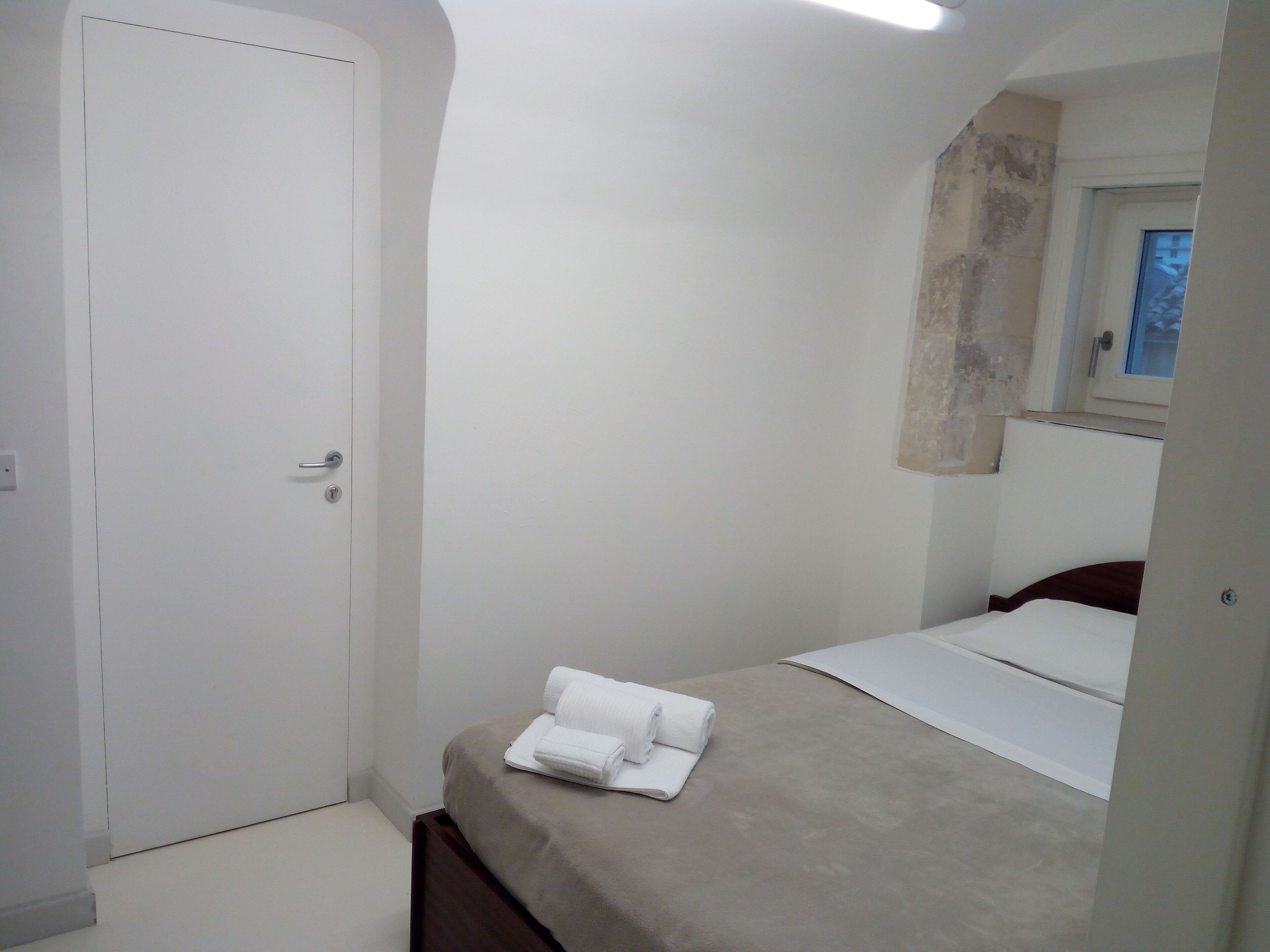 A small, clean room with a bed, a white door, and a window.