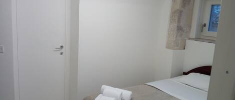 A small, clean room with a bed, a white door, and a window.