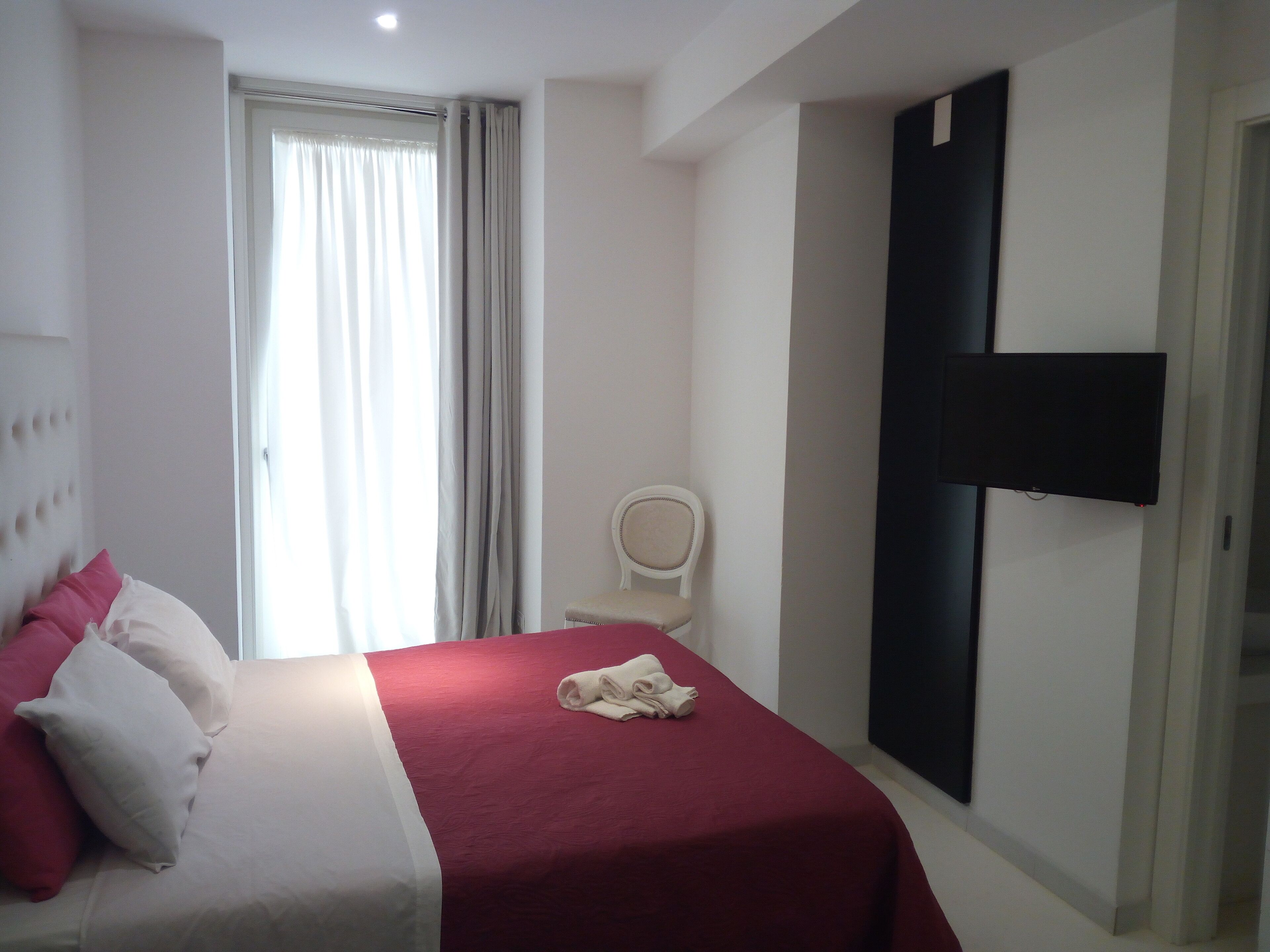 A hotel room with a bed, a chair, a TV, and a window with curtains.