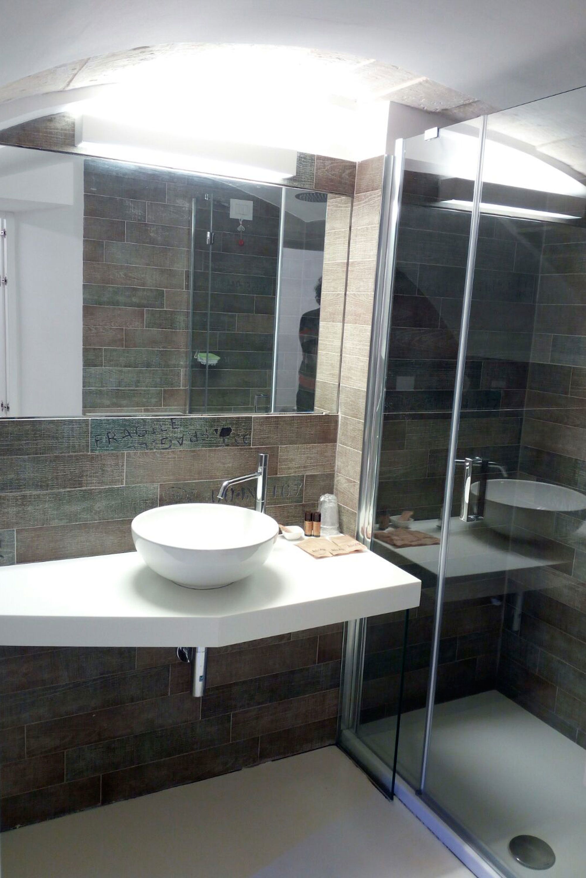 Un bagno moderno con doccia vetrata, lavandino bianco e schienale piastrellato.
