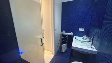 A modern bathroom with a glass shower enclosure, a white sink with a glass basin, and a blue-tiled wall.