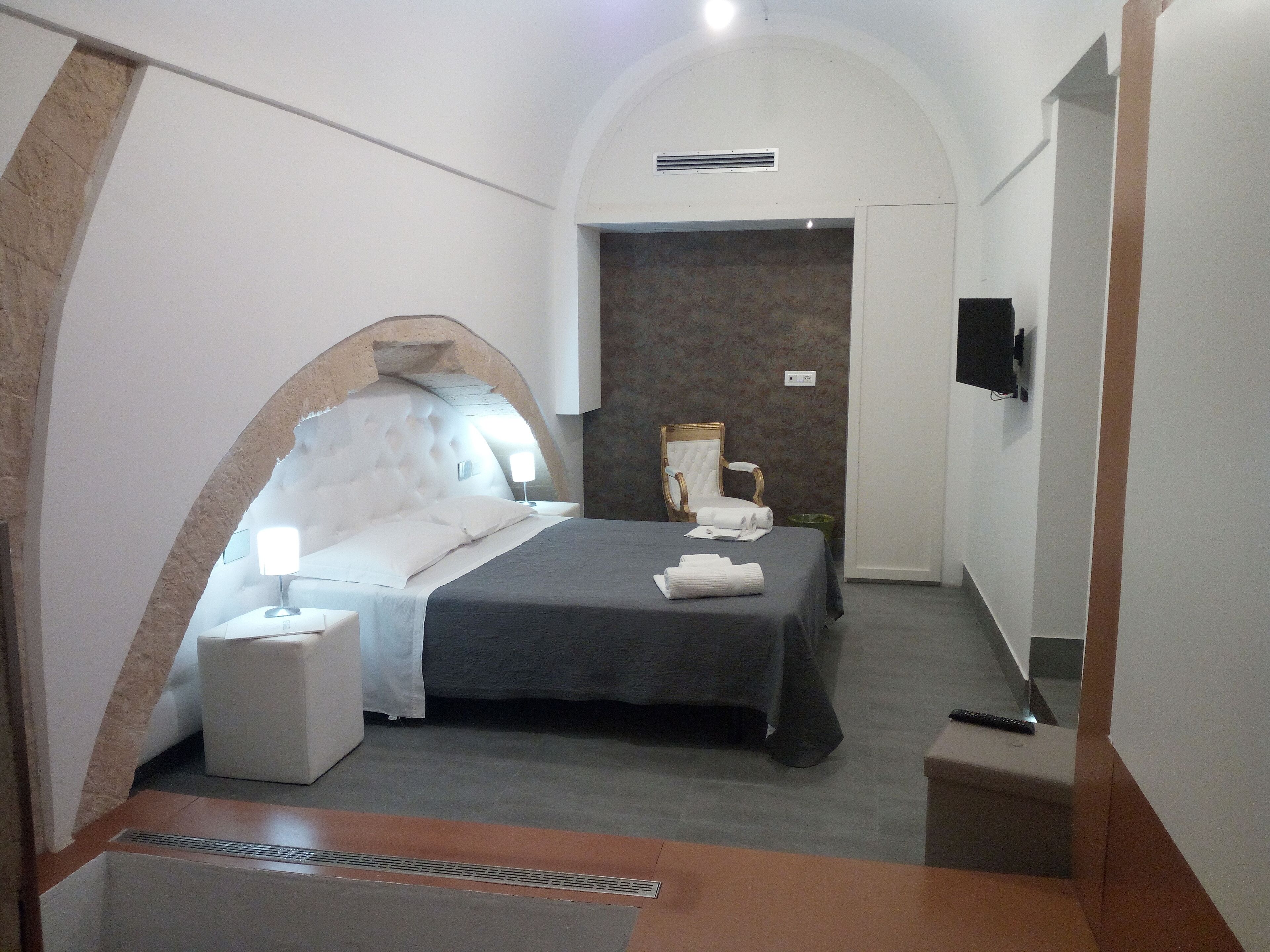 A modern bedroom with a bed, a chair, a TV, and a bathroom area.
