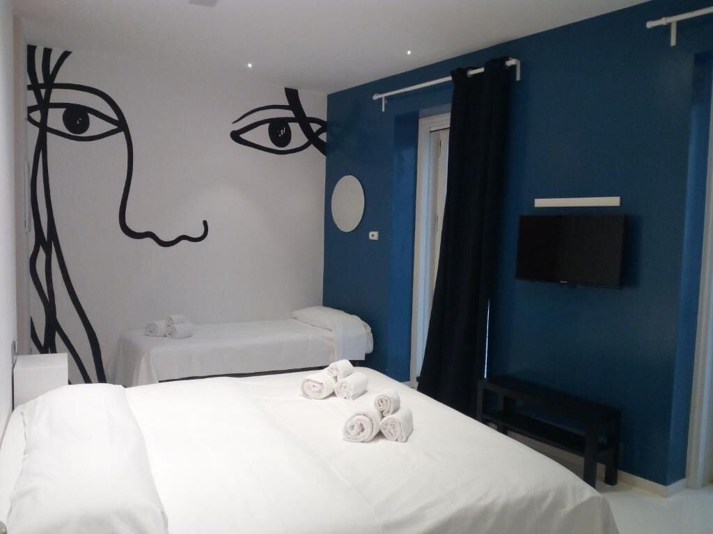 Une chambre d’hôtel avec un lit, un banc, une télévision et un mur décoré d’œuvres d’art abstraites.
