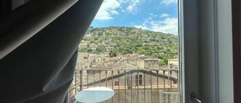 A balcony with a table and chairs, overlooking a hillside with buildings.