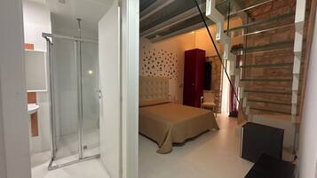 A modern bedroom with a glass shower, a bed with a beige cover, a red wardrobe, and a stone wall.