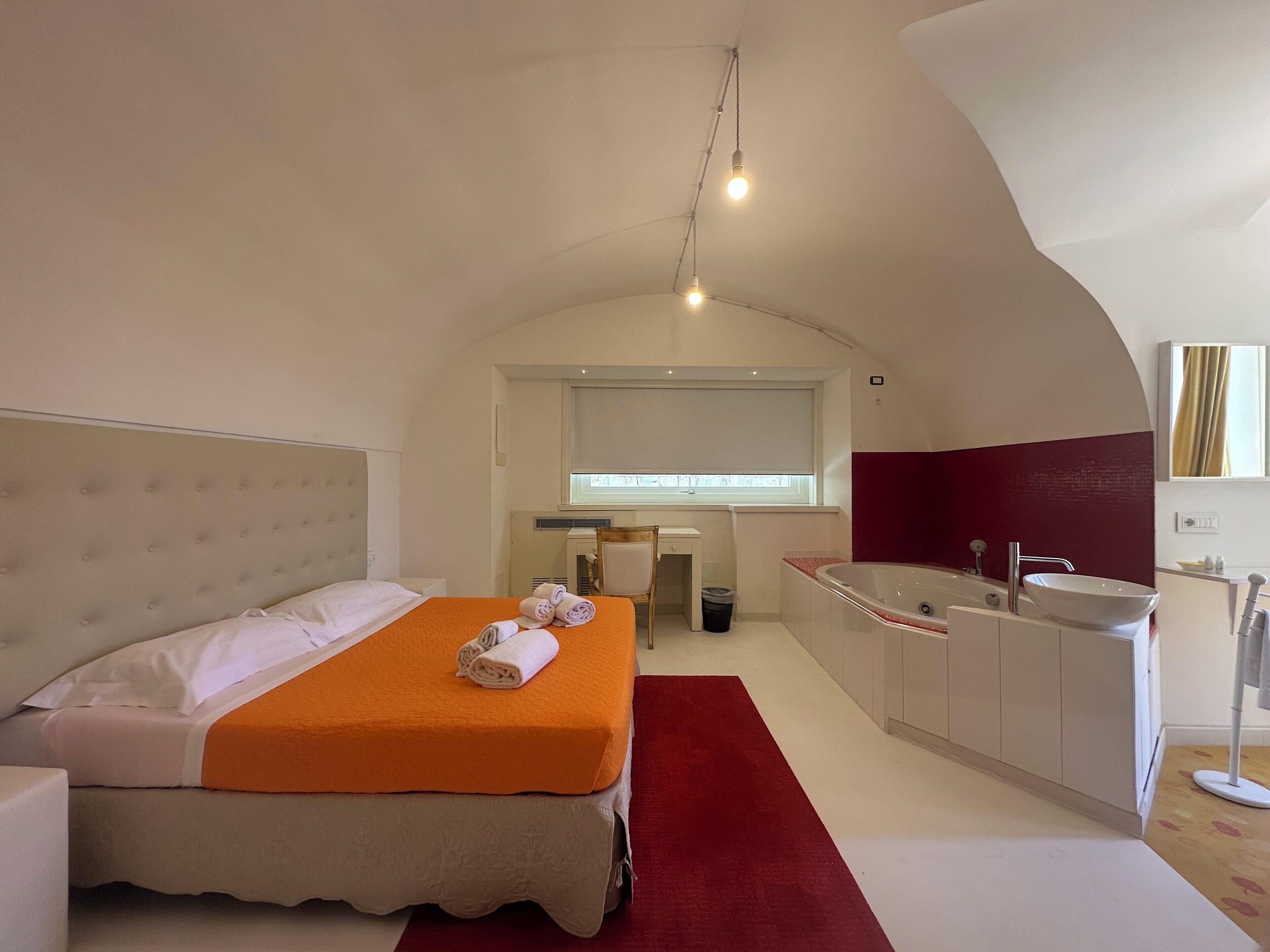 A modern hotel room with a bed, a bathroom with a bathtub, and a window.