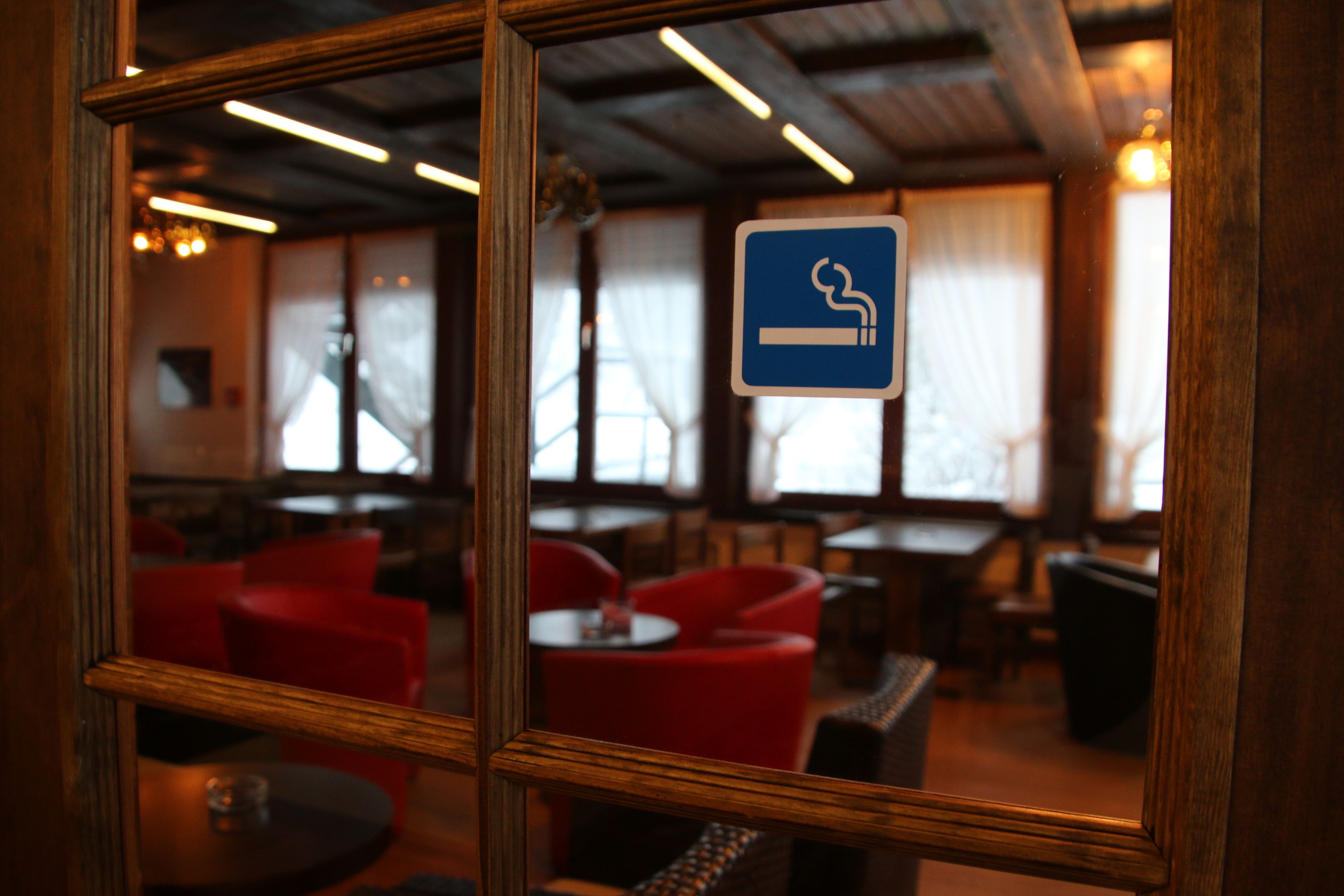 A restaurant interior with red chairs, tables, and a blue smoking sign.