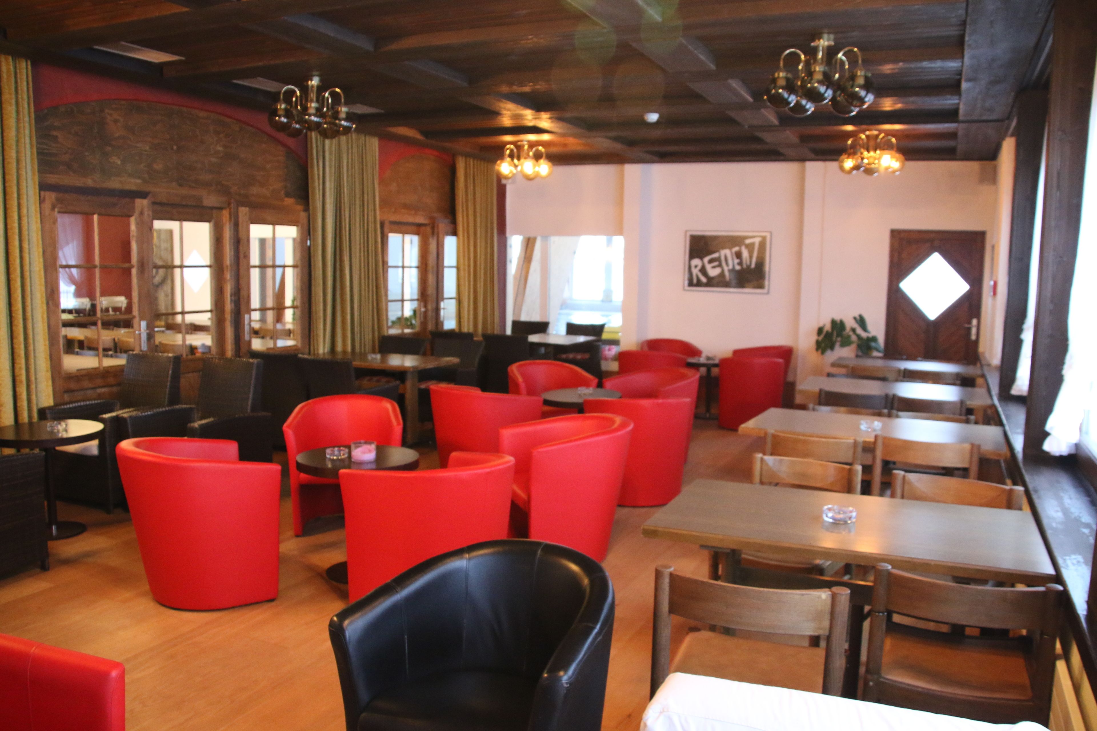 L’intérieur d’un restaurant avec des sièges rouges et noirs, des tables en bois et un plafond rustique.