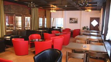 L’intérieur d’un restaurant avec des sièges rouges et noirs, des tables en bois et un plafond rustique.