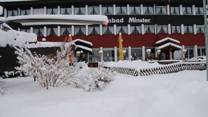 A building with a sign reading "Minster." Snow covers the ground and plants. - Hotel Minster (Unteriberg)