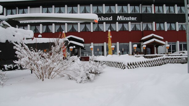 Een gebouw met een bord waarop 'Minster' staat. Er ligt sneeuw op de grond en de planten.