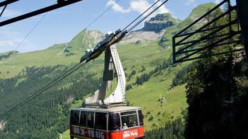 Un teleférico con la marca "HOH-YBRIG", suspendido por cables con montañas al fondo.
