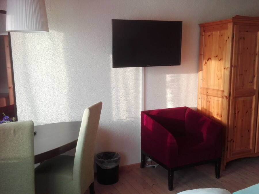 Una habitació amb un armari de fusta, una cadira vermella, un taulell blanc i un televisor negre fixat a la paret.