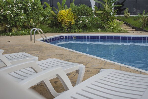 Una piscina con sillas de descanso blancas y borde de azulejos.