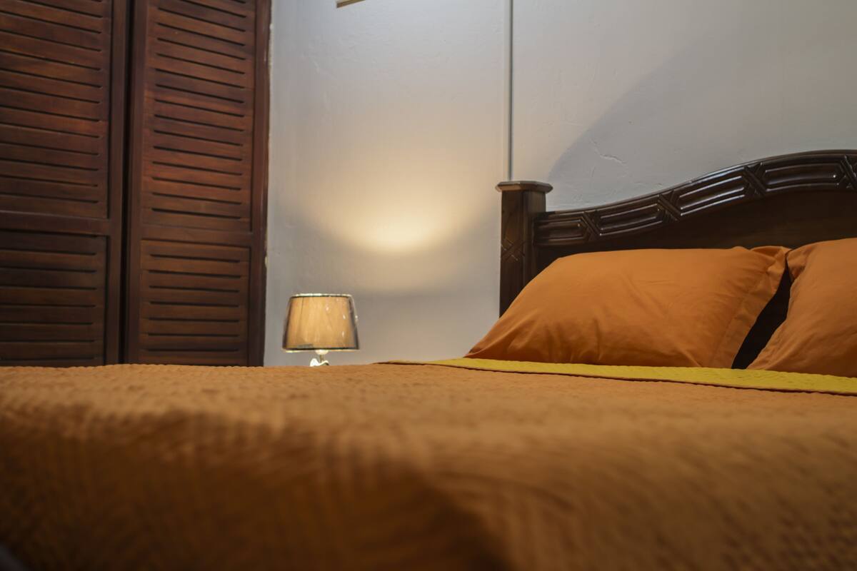 Een bed met een houten hoofdeinde, een lamp op een nachtkastje en een bruine muur.